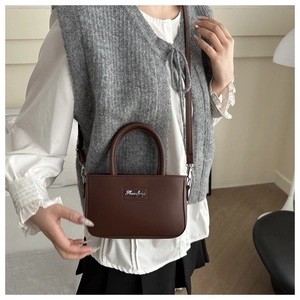 Detail of a dark brown matte leather crossbody bag with silver logo plaque and adjustable strap