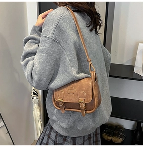 Brown retro shoulder bag with dual metal buckles and adjustable strap on a model