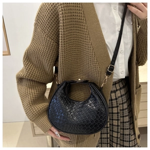 Detail of black woven crescent bag with gold clasp shown on a model in autumn outfit