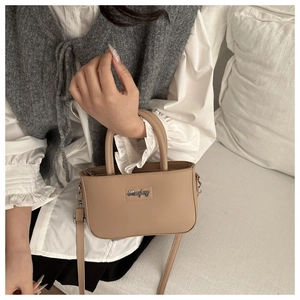 Detail of a khaki crossbody bucket bag showing a metallic logo and textured faux leather