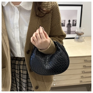 Detail of black woven PU leather crescent bag held by a model in a warm indoor setting