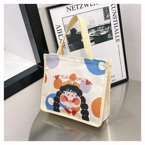 Close-up of cream canvas tote bag with cartoon girl print and yellow woven handles