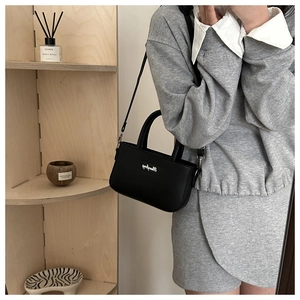Detail of a minimalist black leather crossbody square bag held by a model in a lifestyle setting