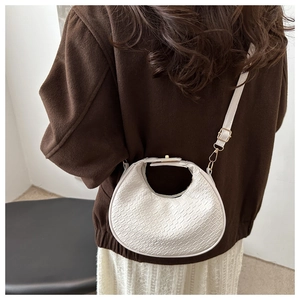 Detail of white woven crescent bag with adjustable strap worn with a stylish wool coat