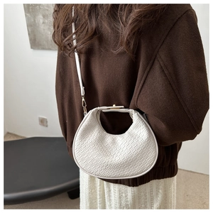Detail of white half-moon crossbody bag with woven texture on a minimalist outfit