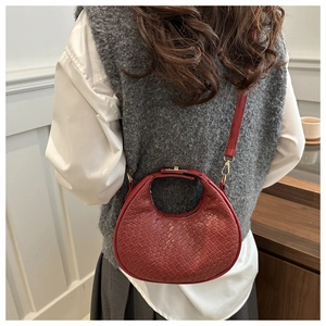Detail of red woven crescent handbag with gold hardware worn by a model in casual style