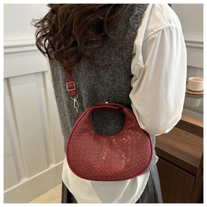 Detailed view of a red woven crescent bag worn over the shoulder by a model indoors