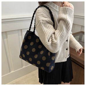 Close-up of deep blue knitted tote bag with golden polka dots and black woven handles