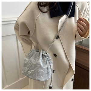 Detail of light blue pleated bucket bag with chain strap and triangle logo on white coat
