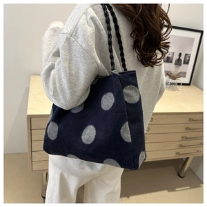 Detail of dark blue polka dot tote bag with thick black braided rope handles on model