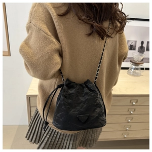 Detail of a black pleated bucket bag featuring a triangle logo and silver chain strap