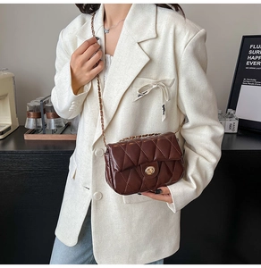 Detailed view of vintage brown quilted chain bag with gold twist lock on a white suit