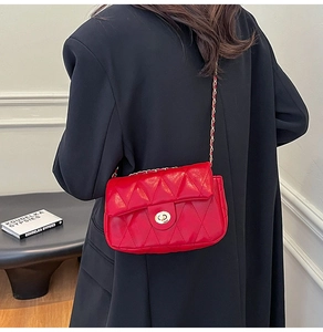 Detail of red quilted crossbody bag with gold chain strap on black blazer