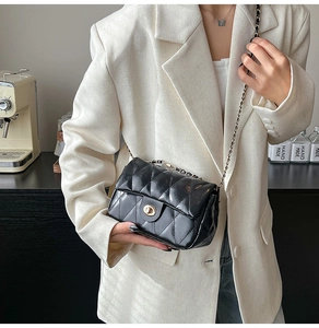 Detail of a black quilted chain shoulder bag with a gold twist lock on a beige blazer
