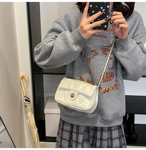 Detail of white quilted crossbody bag featuring a golden twist lock and chain strap