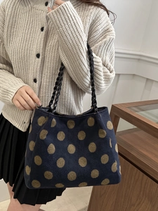 Navy blue polka dot tote bag with woven leather handles on shoulder of model in cozy outfit