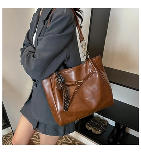 Detail of vintage oil wax leather tote bag featuring metal tennis charm and woven tassel