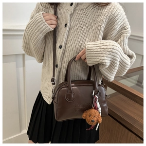 Detail of dark brown leather crossbody bag with letter embossing and plush puppy charm