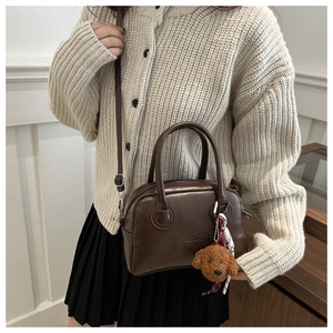 Detail of dark brown leather crossbody bag with letter embossing and plush teddy pendant