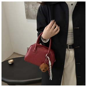 Macro detail of red leather Boston bag with embossed logo and plush teddy bear charm