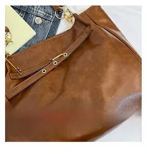 Detailed close-up of brown oil wax leather tote bag texture with gold hardware and stitching