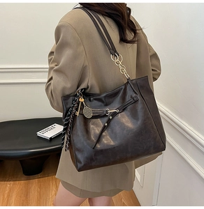 Detail view of large brown oil wax leather tote bag with gold charm on a model