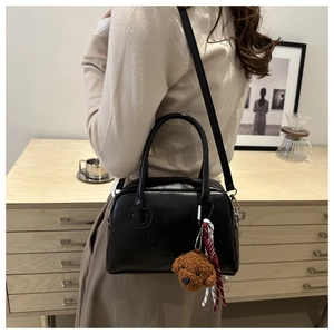 Detail of black matte leather Boston bag with embossed text and plush teddy bear charm
