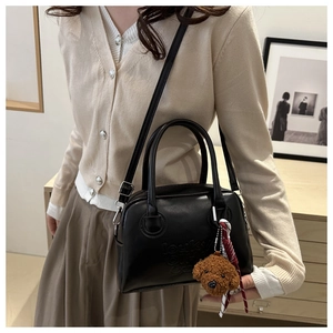 Detail of black leather bag with embossed letters and a cute brown teddy bear charm