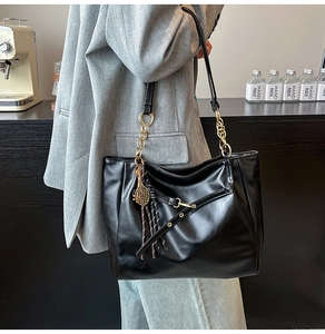 Detail of black vintage oily leather tote with golden chain and tennis racket charm