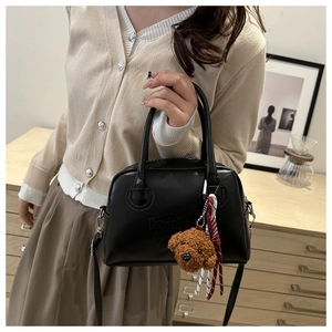 Detail of black Boston leather handbag with logo embossing and cute bear pendant accessory