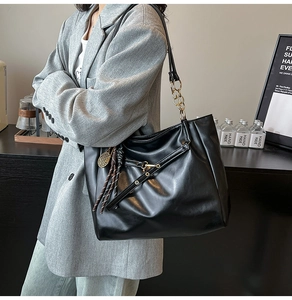 Detail of black wax leather tote bag featuring golden chain strap and unique tennis charm