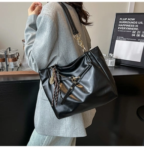 Close-up of black oil wax leather tote with golden chain strap and tennis racket charm