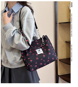 Detail of black canvas tote bag featuring red cherry print and metal chain strap
