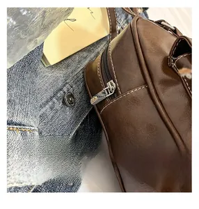 Detail of brown faux leather shoulder bag with white contrast stitching and metal zipper