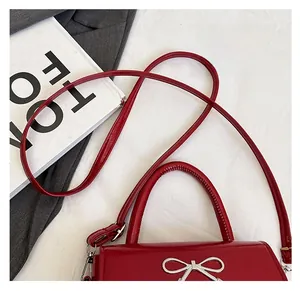 Detail of red glossy patent leather handbag with silver bow buckle and shoulder strap