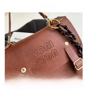 Nahaufnahme von braunem Leder mit Lychee-Maserung, Logo-Prägung und Metallring-Details