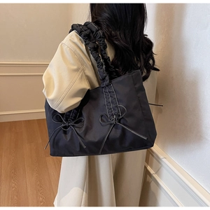 Vue latérale d'un sac cabas noir avec des nœuds et une bandoulière plissée stylée