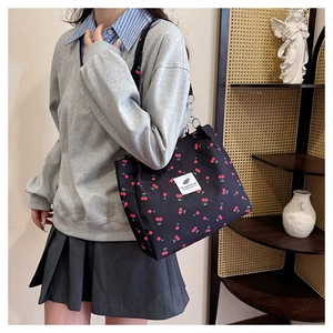 Detail of black canvas tote bag featuring red cherry print and white text patch