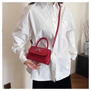 Detail of red patent leather crossbody bag with silver bow ornament and slim handle