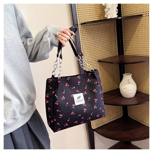 Detail of canvas tote bag featuring red cherry print and silver metal chain strap handle