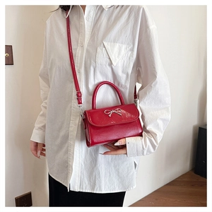 Detail of red glossy patent leather handbag featuring a silver metallic bow and strap