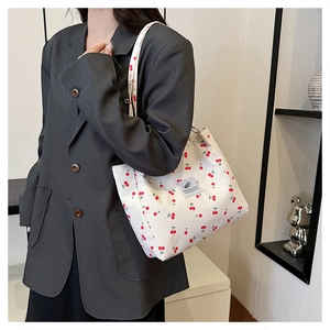 Detail of white canvas tote bag with cherry print and woven label on grey suit