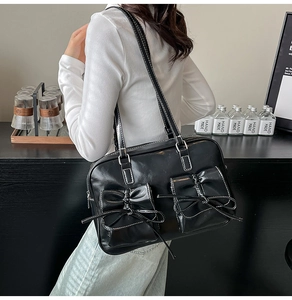 Detail of black glossy leather shoulder bag with large bows and contrast white stitching