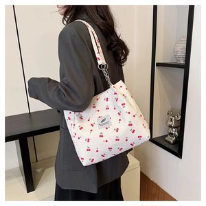 Close-up of canvas tote bag with cherry print and metal chain strap on a model