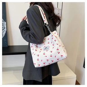 Detail of white canvas tote bag with cherry print and metallic chain strap on shoulder