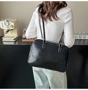Detail of black glossy shoulder bag with white contrast stitching and dual straps