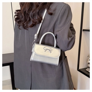 Detail of silver mini crossbody bag featuring a metallic bow and sleek polished finish