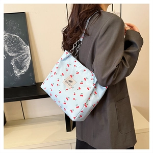 Detail of light blue cherry print tote bag featuring a purple label and chain strap
