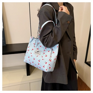 Close-up of light blue canvas tote bag featuring red cherry prints and metal chain detail
