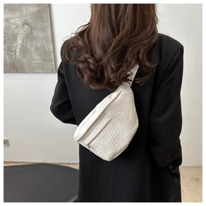 Détail d'un sac de poitrine blanc en cuir tressé avec fermeture dorée sur veste noire